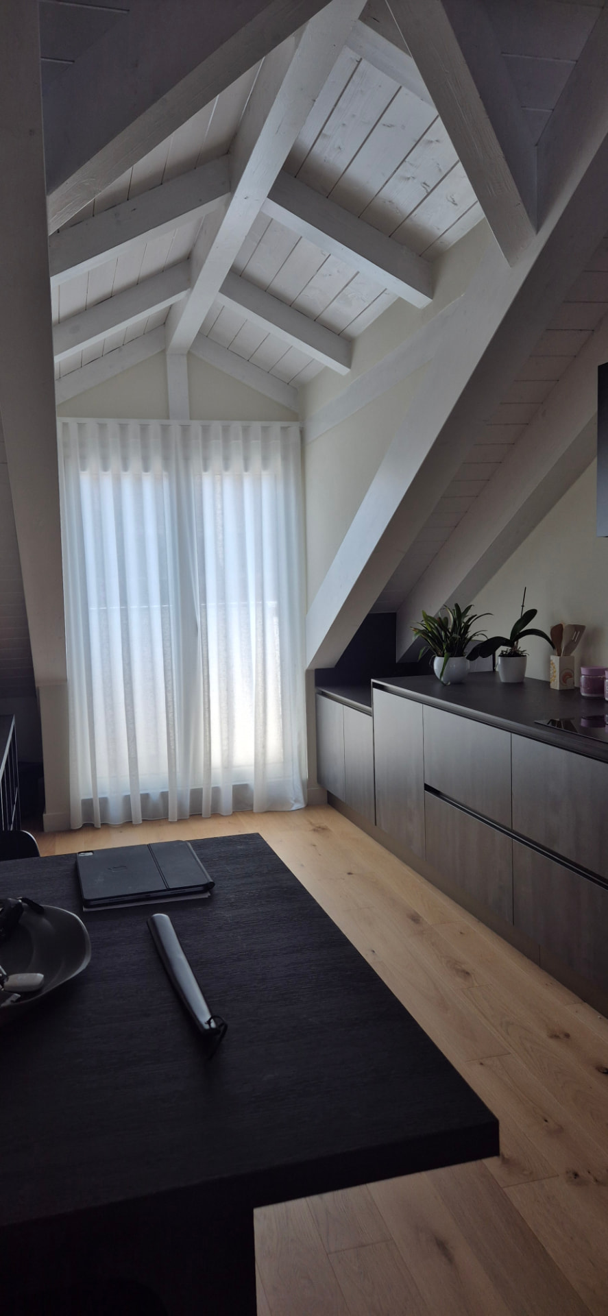Mansarda contemporanea con travi a vista e tendaggio bianco a tutta altezza