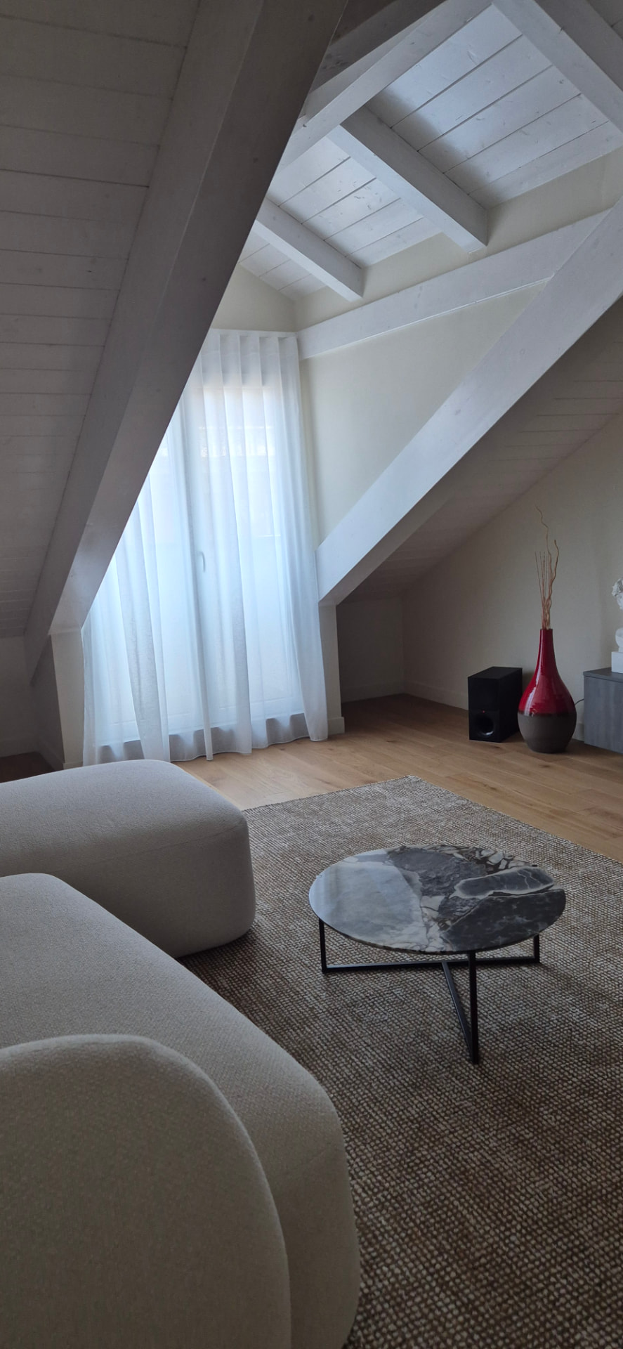 Zona living mansardata con tendaggio leggero e arredi dalle forme morbide